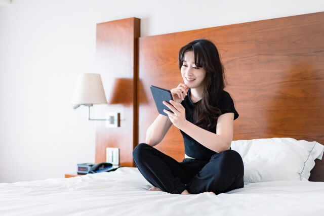 ベッドでタブレットを操作する女性
